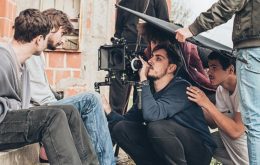 A production crew filming a-roll of two actors sitting outside on a window sill