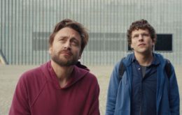 Two white men, one wearing a red hoodie and one wearing a blue zip-up, gaze upward.