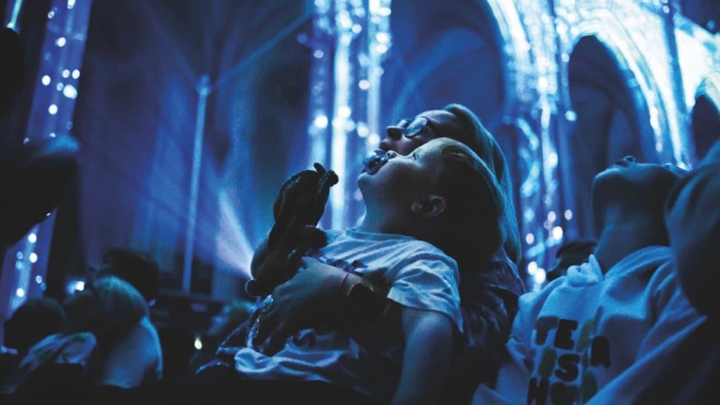 A parent and child looking up at a projection on the roof of a cathedral