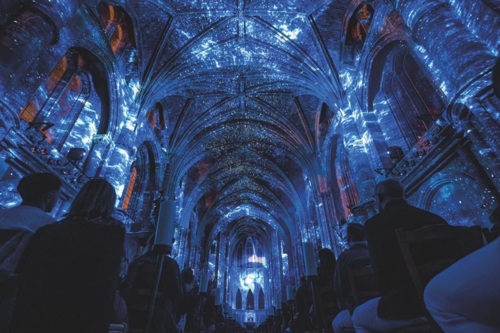 A projection of the blue night sky and stars on the ceiling of a cathedral