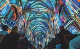 Light projections on the roof of a cathedral with people sitting in the pews