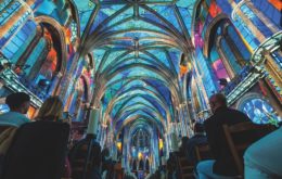 Light projections on the roof of a cathedral with people sitting in the pews