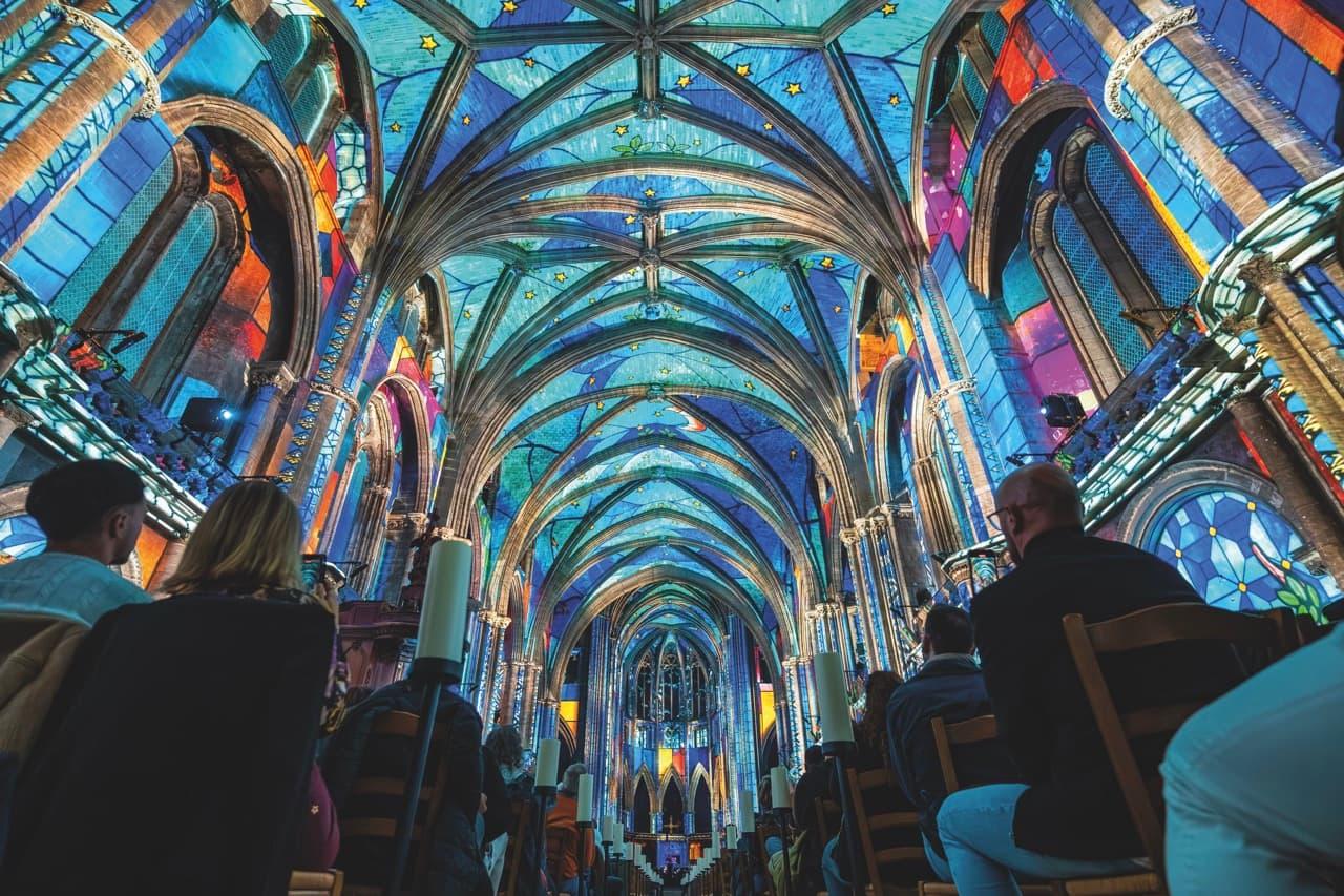 Light projections on the roof of a cathedral with people sitting in the pews
